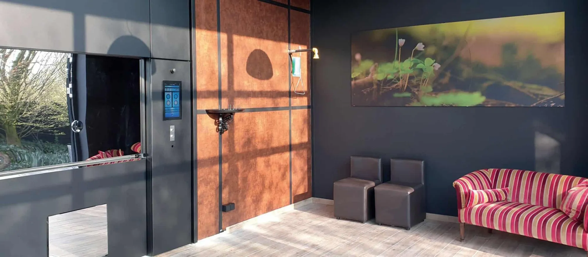 The insertion room of Cremaere crematorium in Almere: the black front of the DFW cremator with its touchscreen, a copper wall and a striped sofa